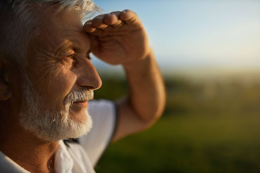 Older man outdoors shading his eyes with his hand while looking into the distance