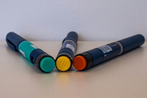 Three medical injection pens with colored caps placed on a table