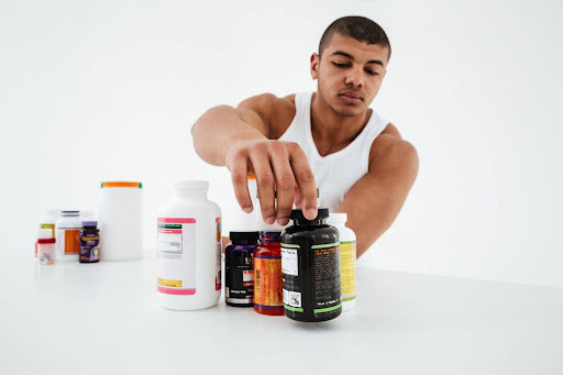 Man reaching for a bottle of dietary supplements among several vitamin containers on a table.