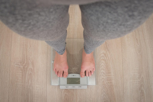 Person standing barefoot on a digital scale on a wooden floor.